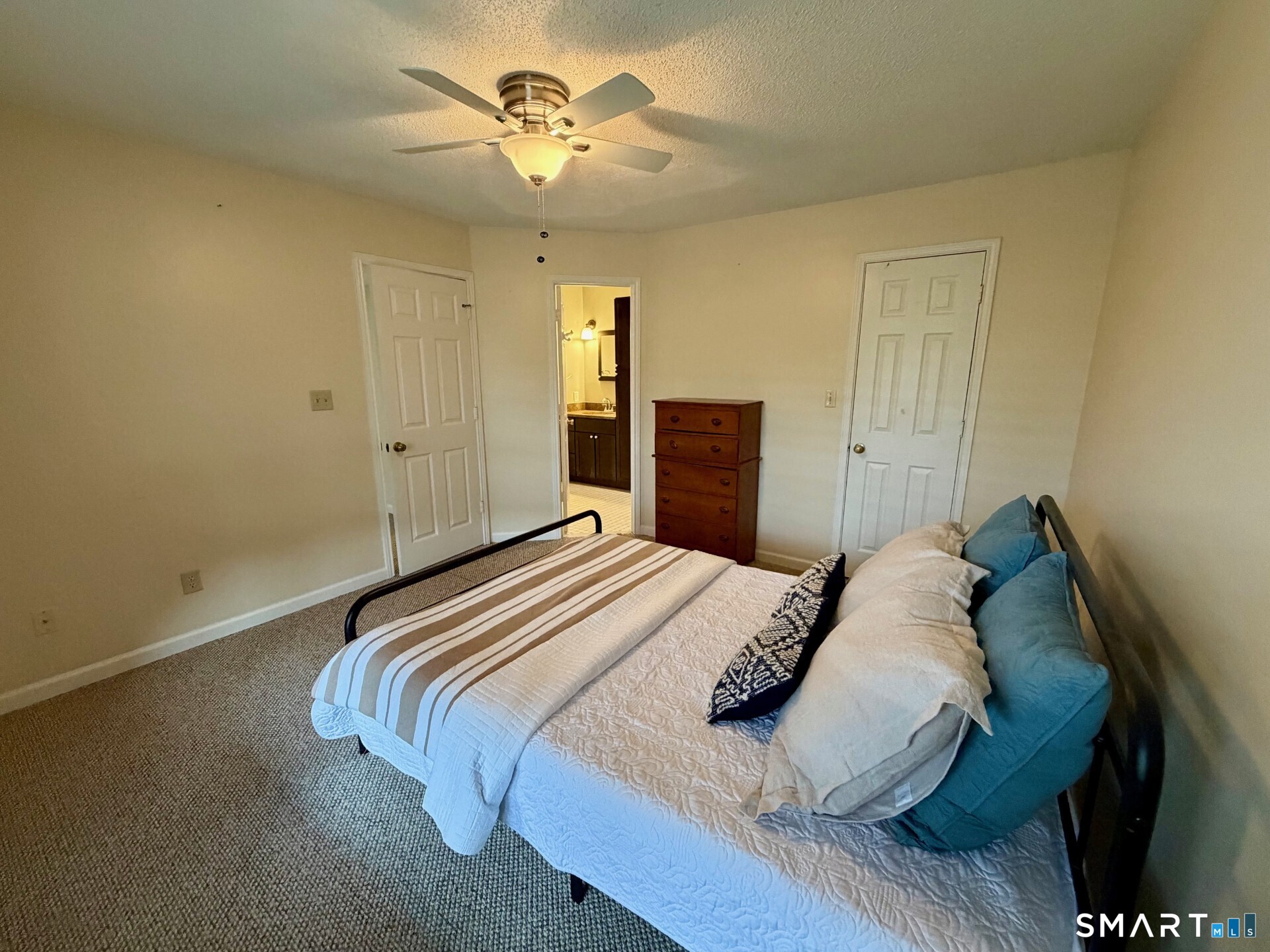 Furnished bedroom with blue accent pillows, a wooden dresser, and an open doorway to the bathroom.
