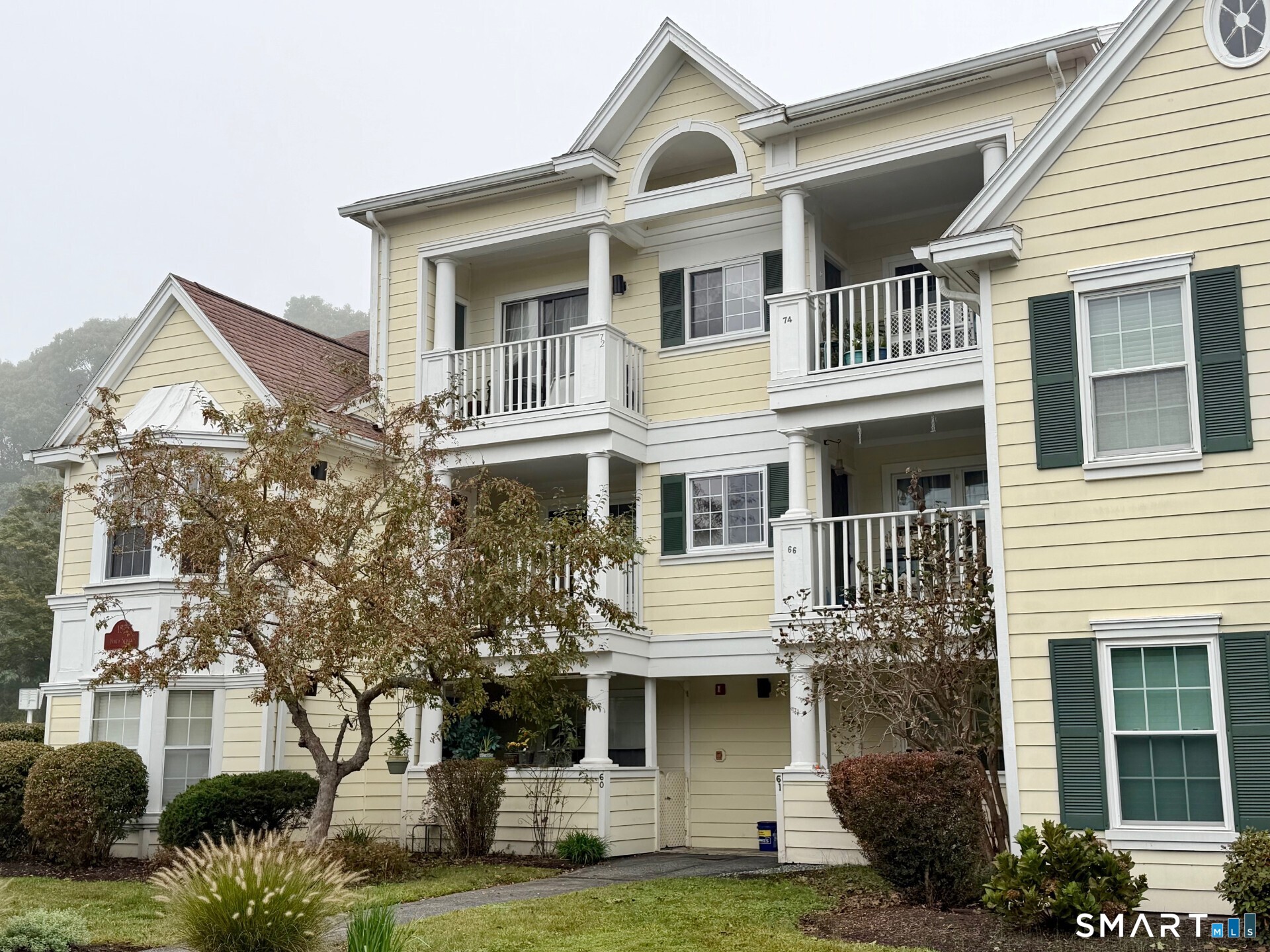 Pale yellow condominium building with white columns, stacked balconies, and landscaped grounds.