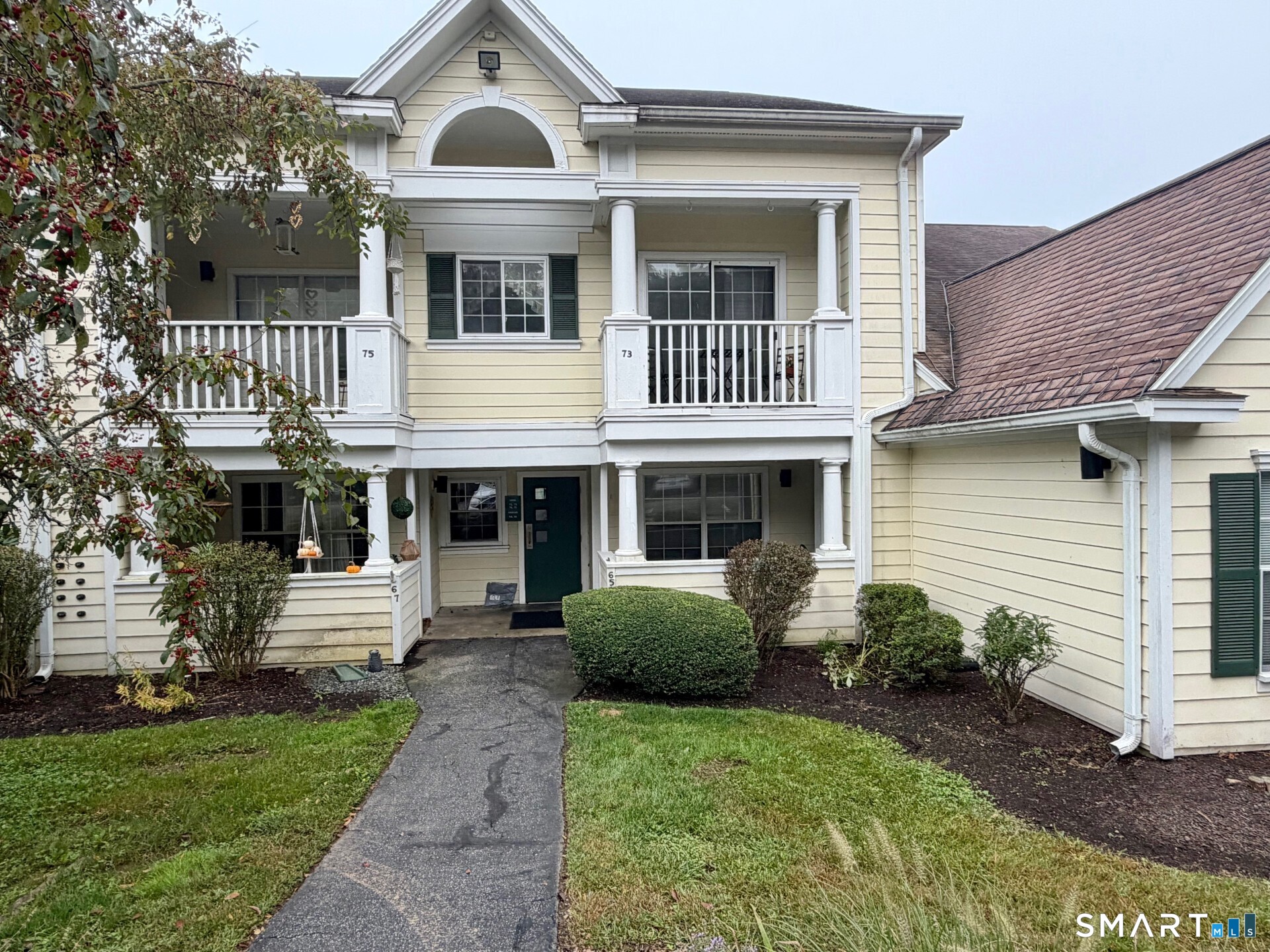 Pale yellow multi-unit home with white columns, covered balconies, and a walkway through the lawn.