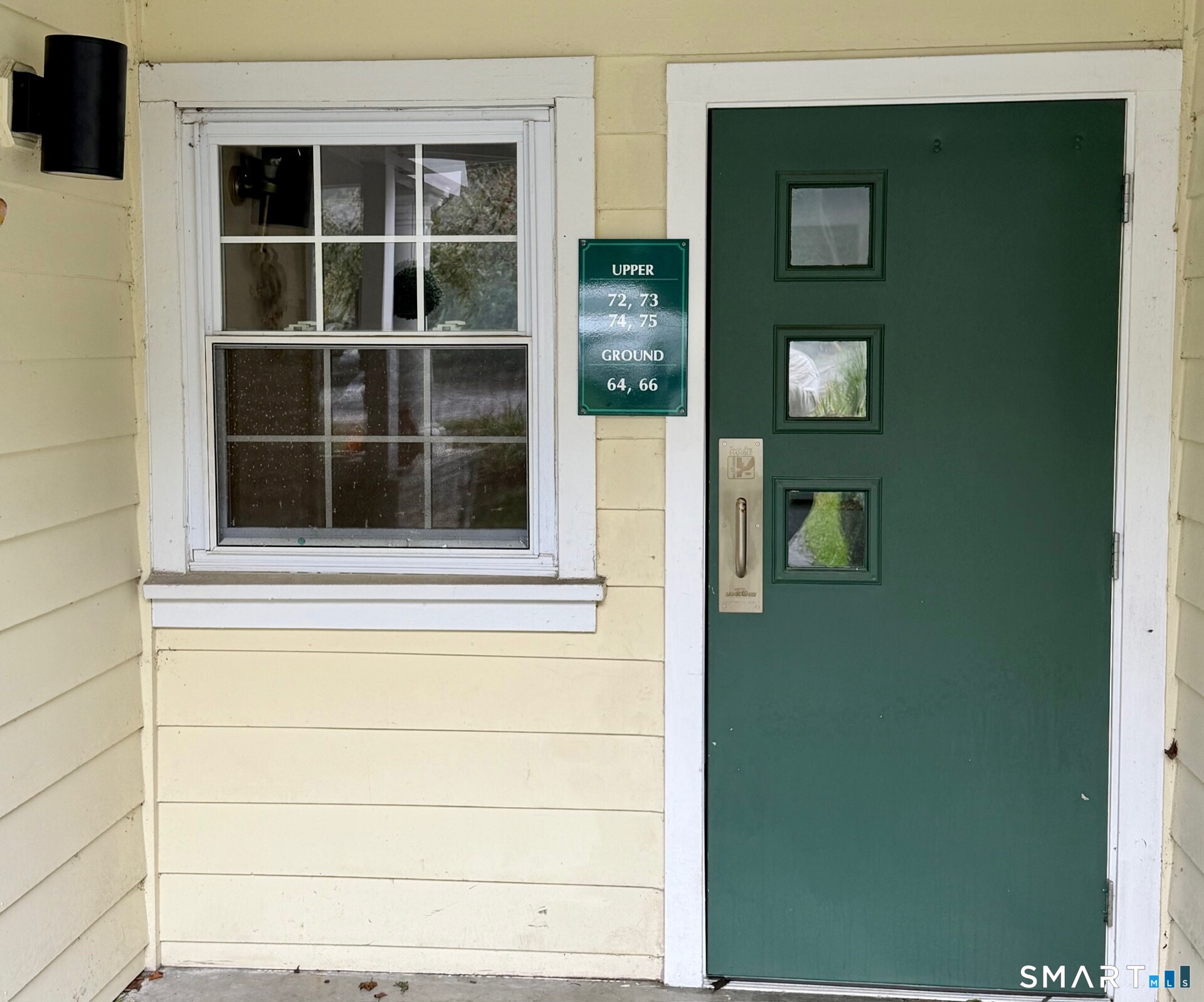 Residential entrance with a dark green, three-window door and a sign listing ground-floor units.