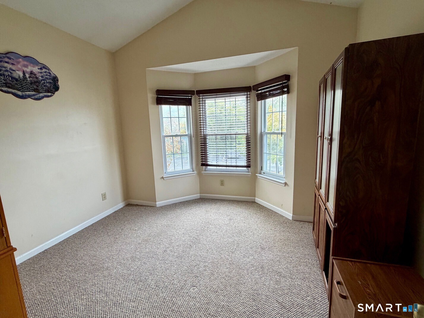Carpeted room with a three-window bay and tall dark wood built-in cabinets.