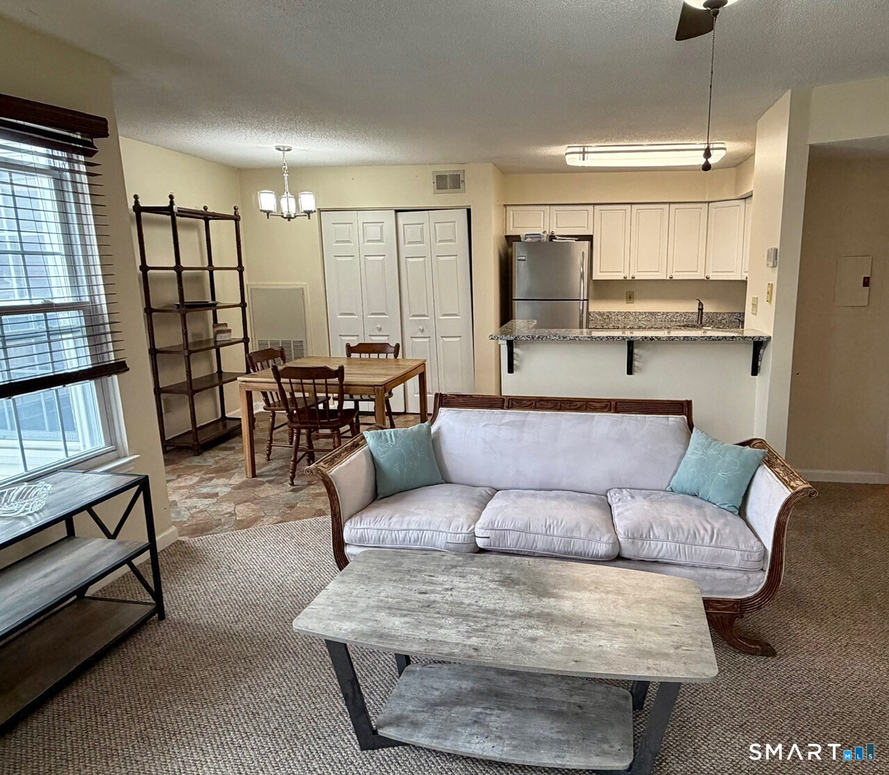 Living room with a white sofa, opening to a dining area and kitchen with a breakfast bar.