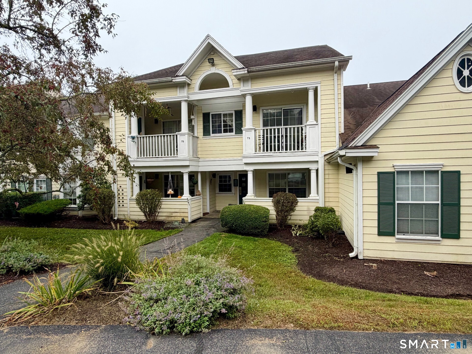 Pale yellow condominium building with stacked porches, green shutters, and landscaped walkway.