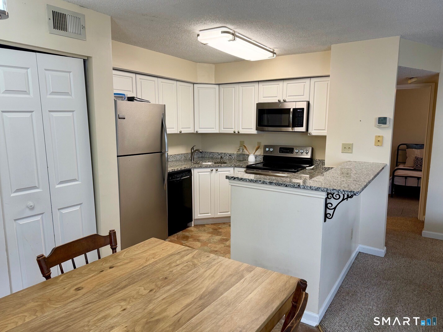 Kitchen with white cabinets, granite counters, stainless steel refrigerator, and peninsula with decorative brackets.