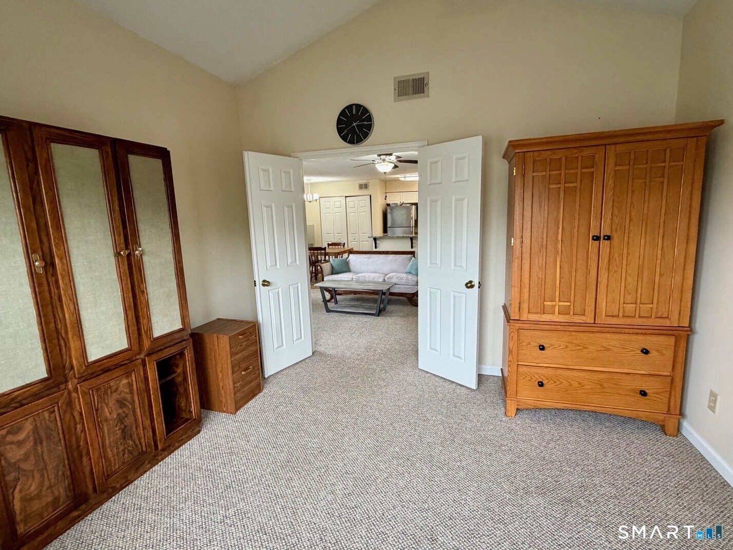 Bedroom with wooden wardrobes and open double doors overlooking a living room and kitchen.