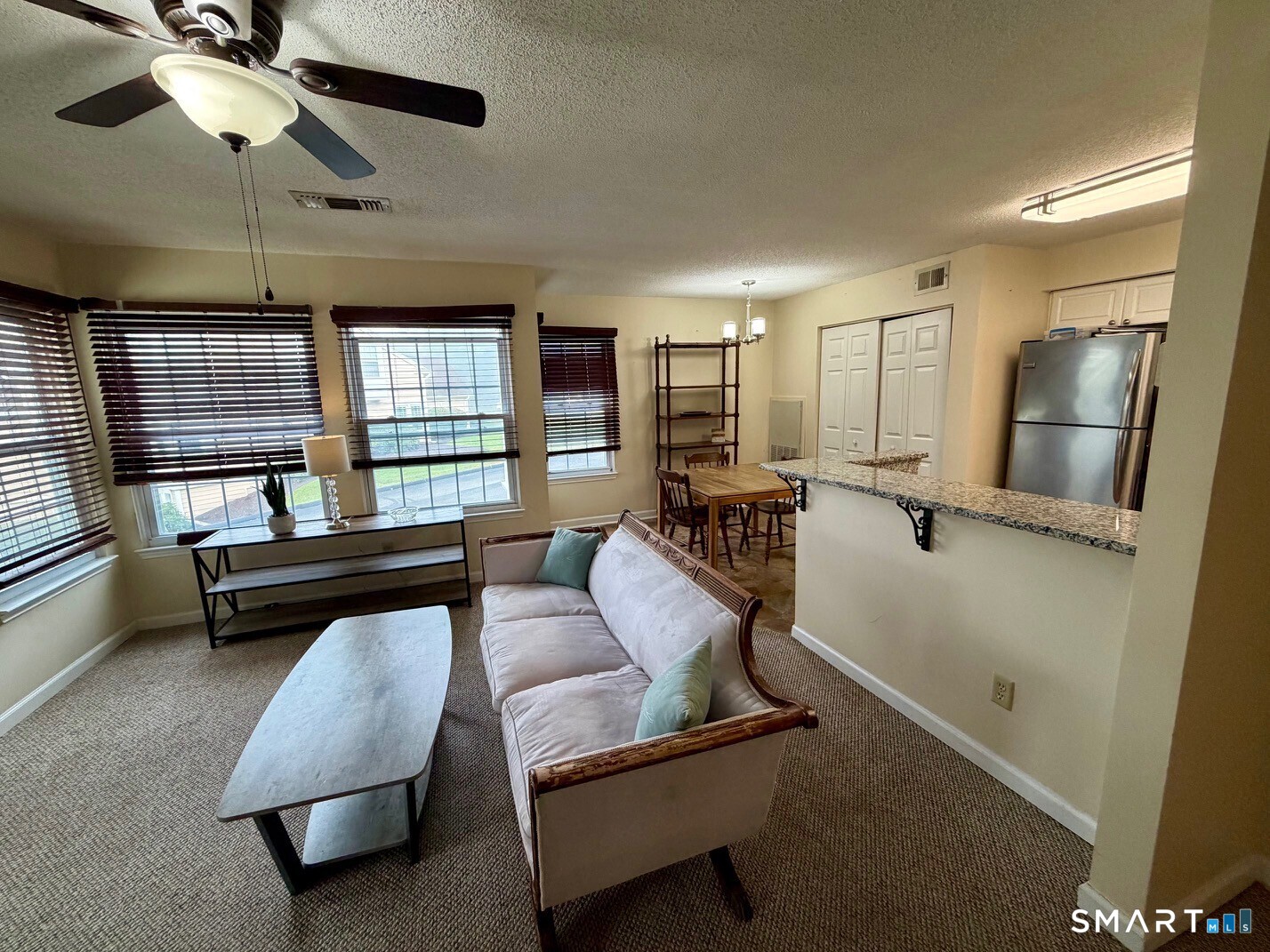 Living room with a pale sofa, broad windows, and an open dining and kitchen area.