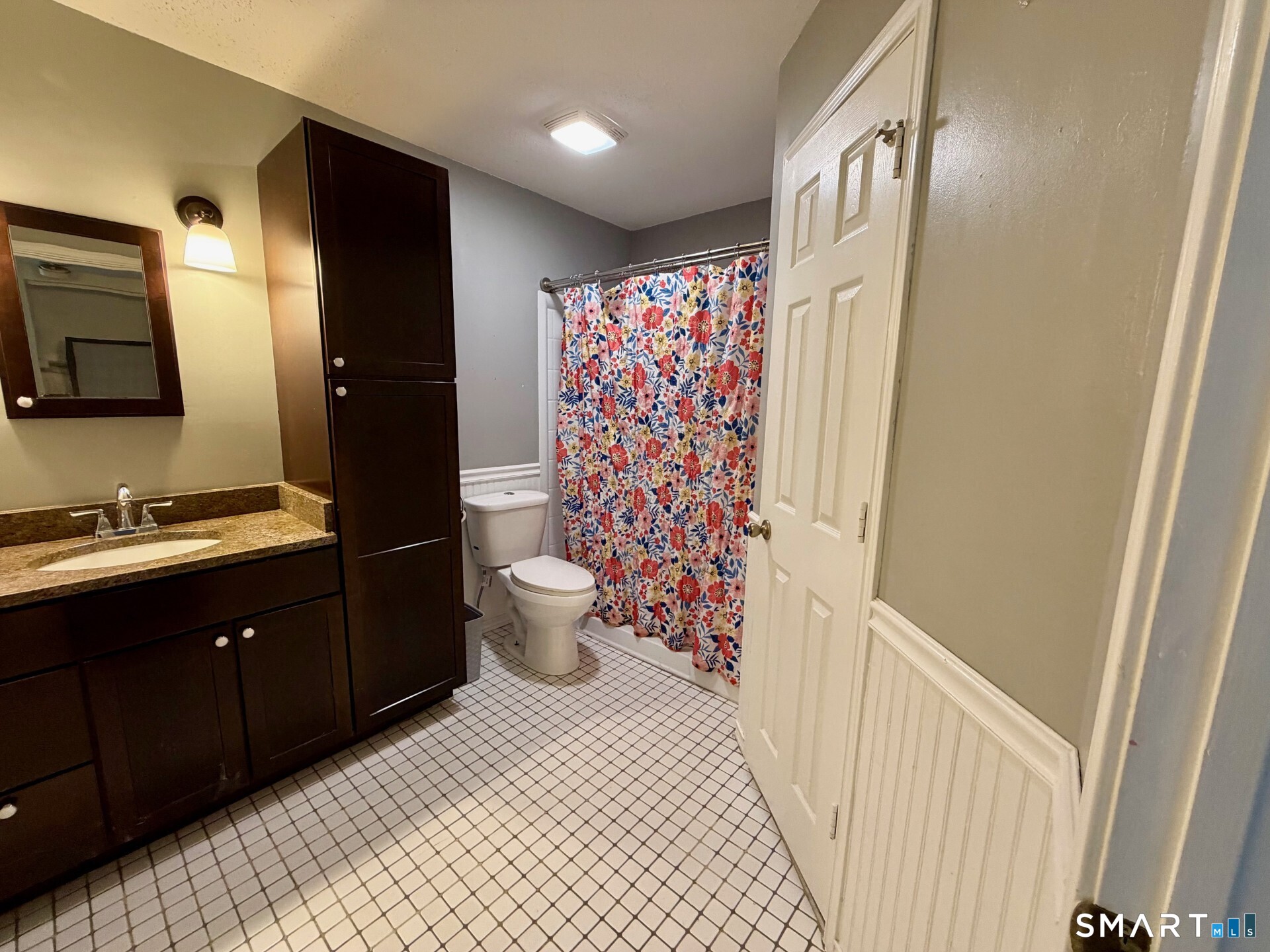 Bathroom with dark wood vanity, granite countertop, floral shower curtain, and square-tile floor.