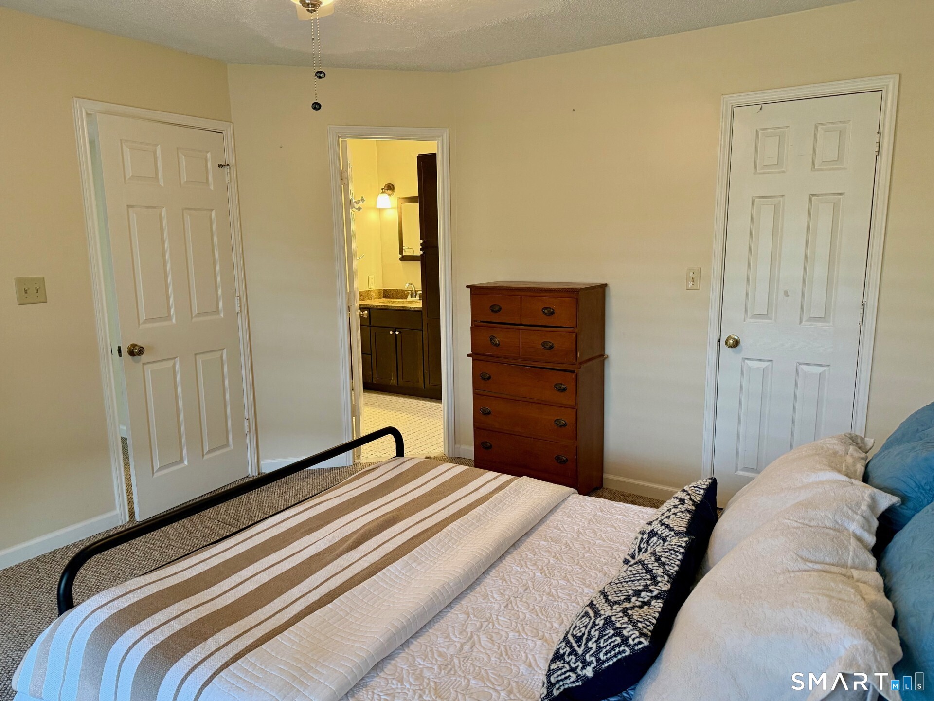 Bedroom with a striped bedspread, wooden dresser, and open doorway to an en-suite bathroom.