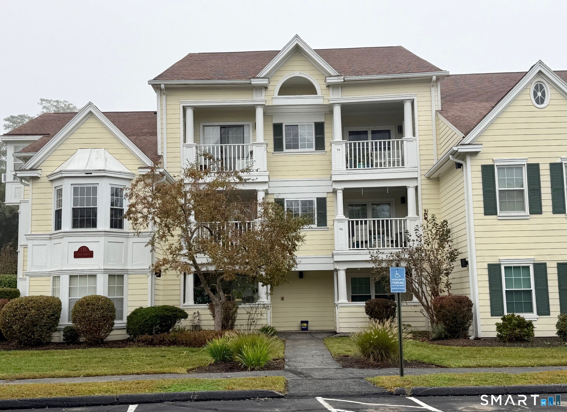 Pale yellow multi-unit building with white-trimmed balconies and landscaped lawn.