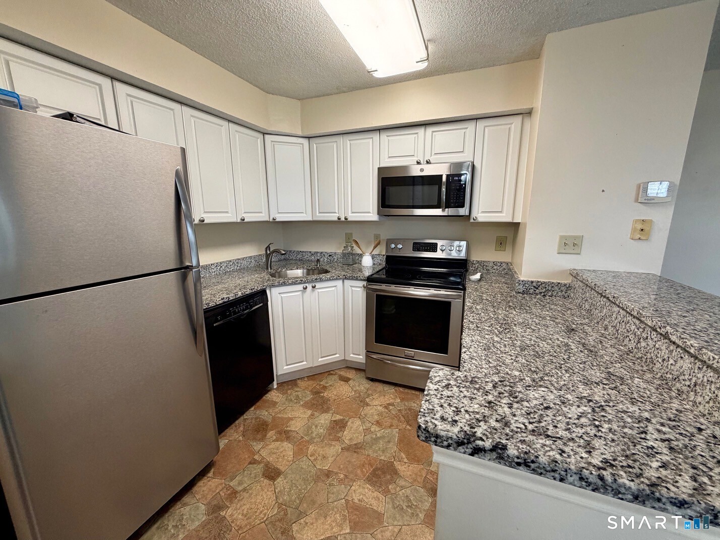 Kitchen with white cabinets, granite countertops, stainless steel appliances, and patterned tile flooring.