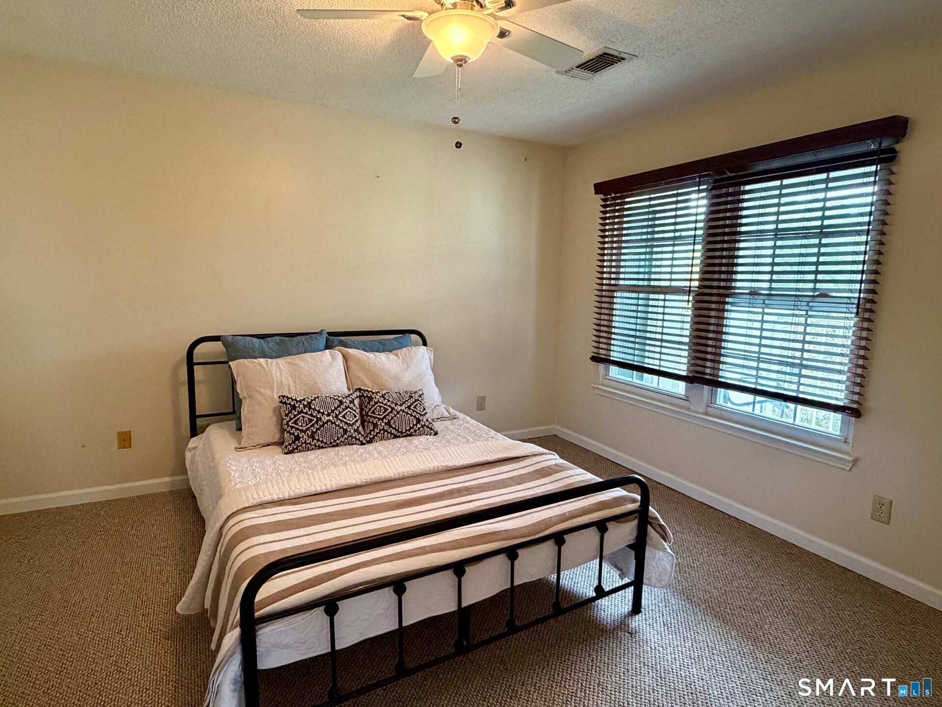 Furnished bedroom with a black metal bed and two windows with dark blinds.