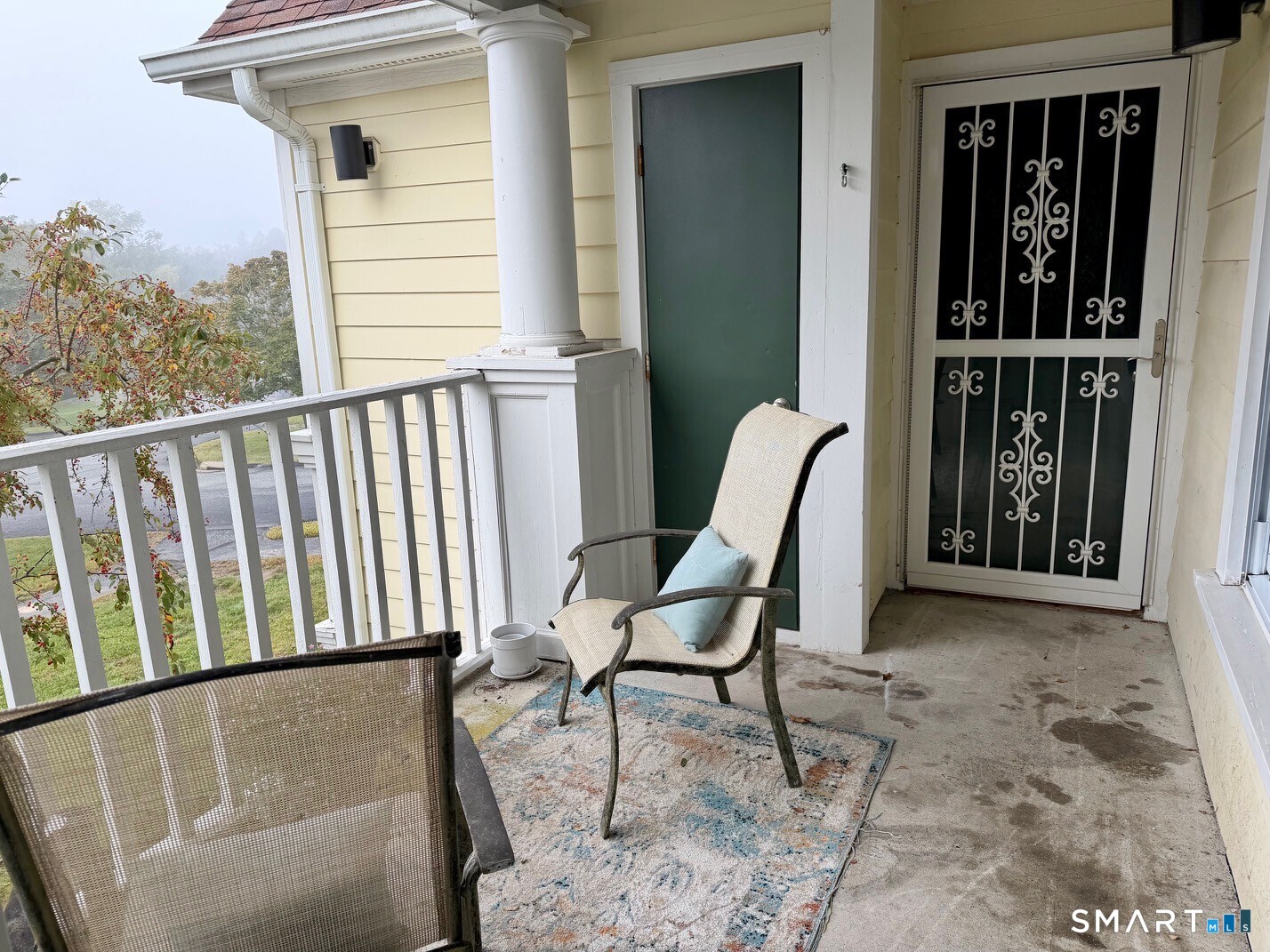 Covered porch with white railing, green entry door, metal security door, and two chairs.
