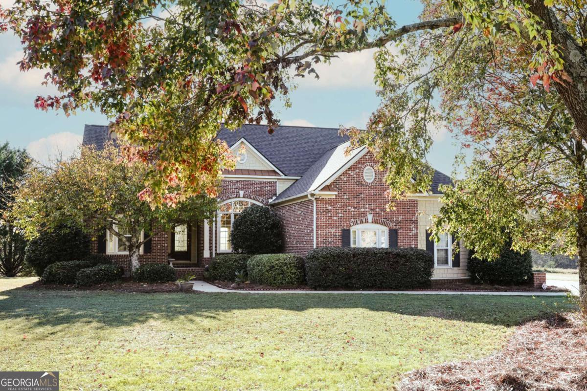 Brick-and-siding house framed by autumn trees, with a broad lawn and landscaped shrubs.