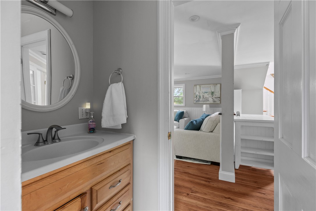 Bathroom vanity with a round mirror and wood cabinets overlooking a furnished living area.