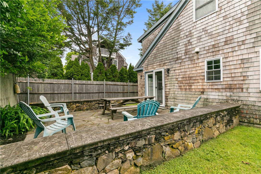 Stone patio beside a shingle-sided home, furnished with Adirondack chairs and a picnic table.