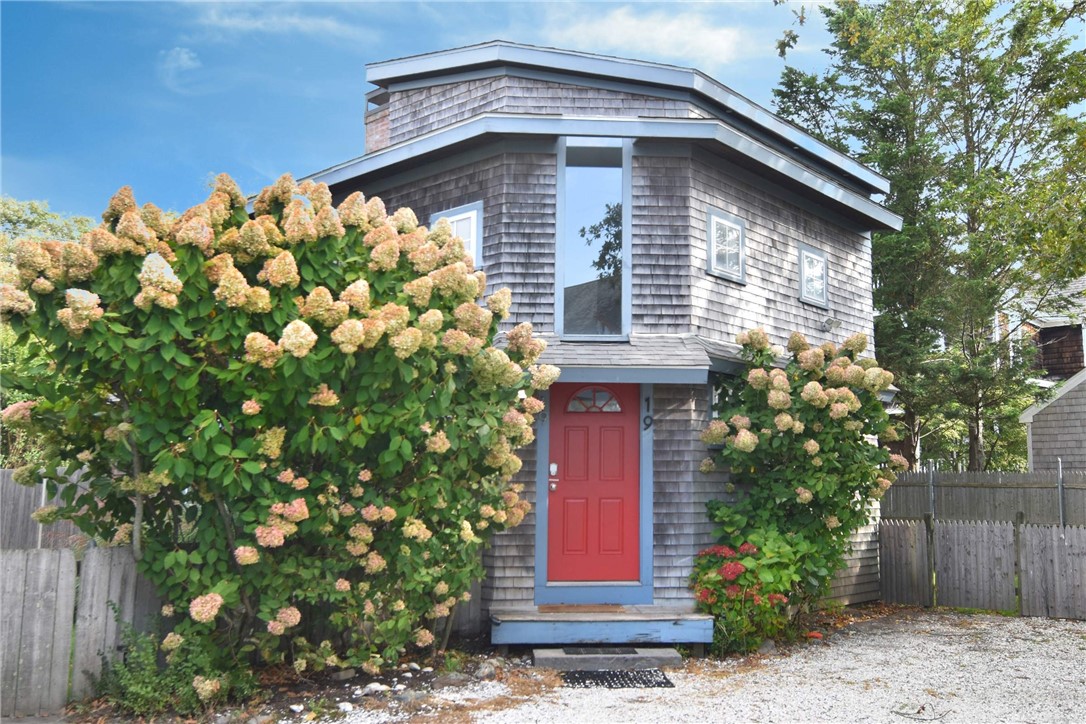 Gray shingle house with a red front door framed by blooming hydrangeas.