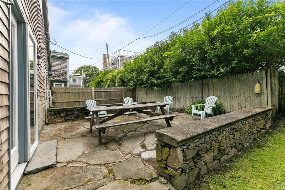 Stone patio with a picnic table and Adirondack chairs beside a shingled home.