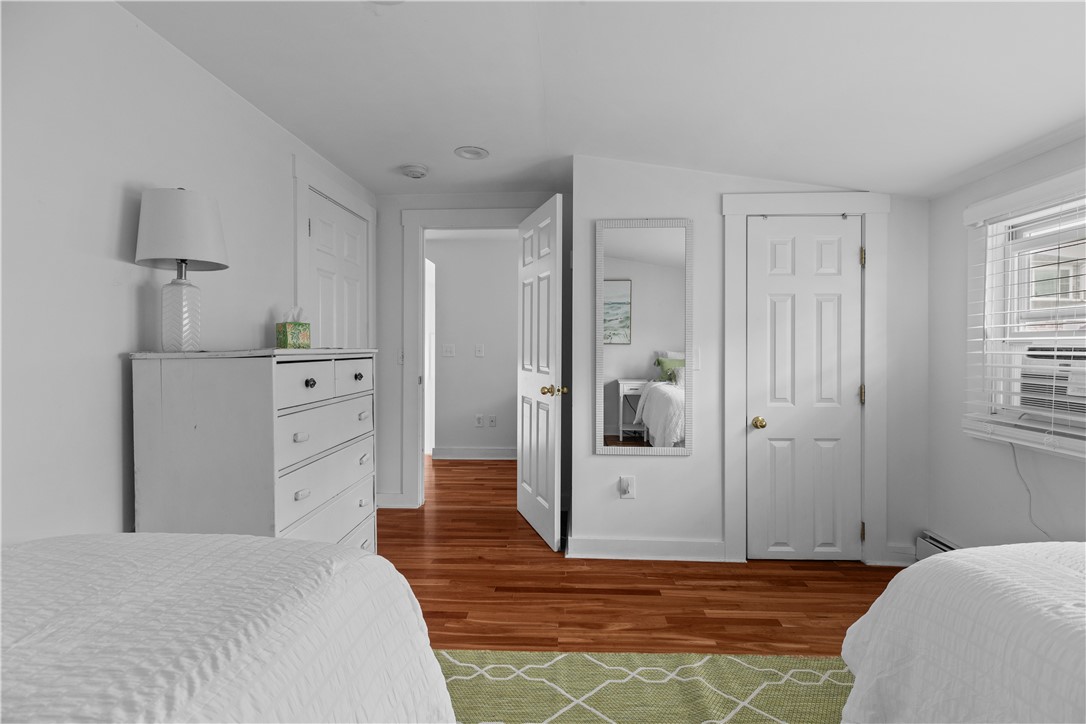 Bedroom with two beds, a white dresser, hardwood floors, and a window with blinds.