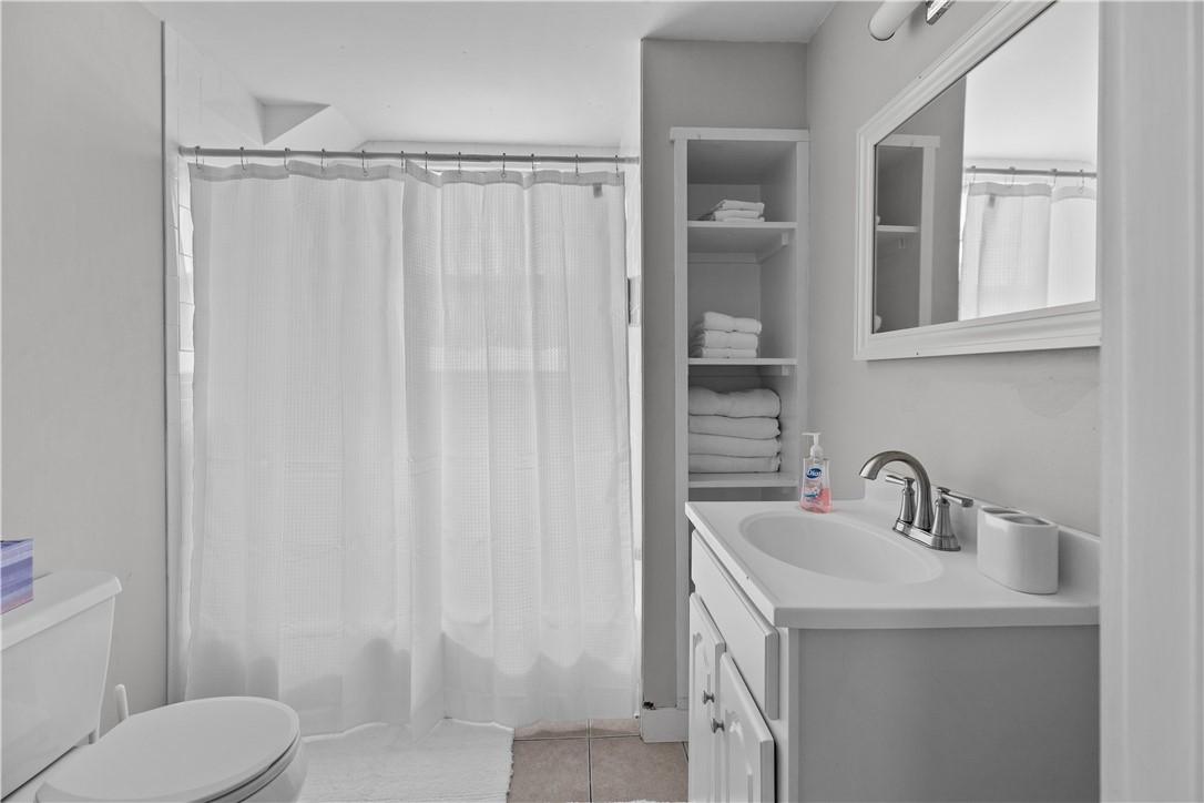 Bathroom with a white vanity, framed mirror, curtained shower, and open shelves of folded towels.