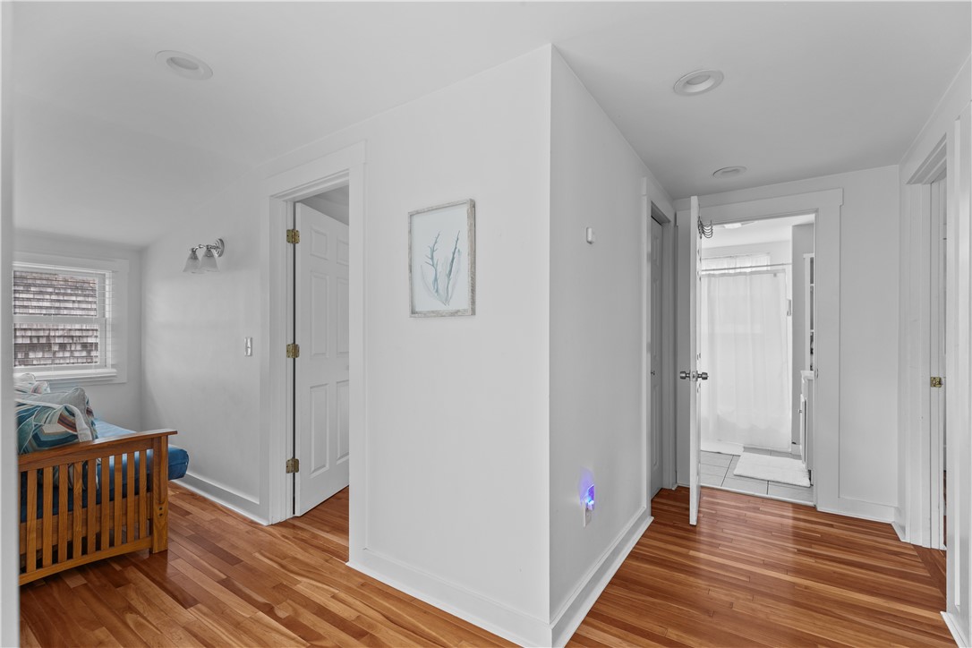Hallway with warm hardwood floors, open doors, and a glimpse of a sitting area and bathroom.