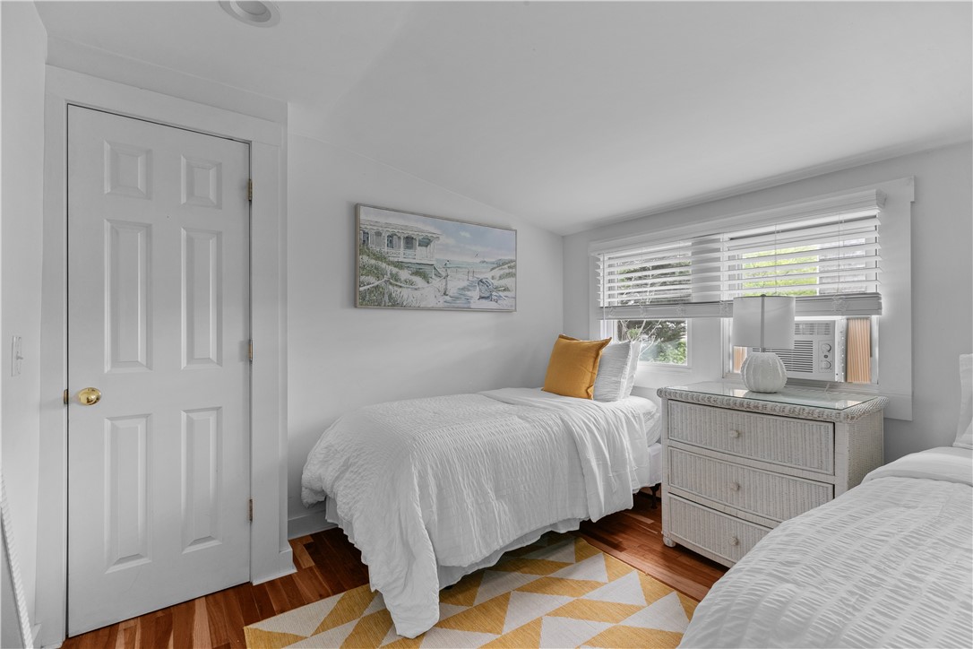 Bedroom with two single beds, white bedding, hardwood floors, and a window air conditioner.