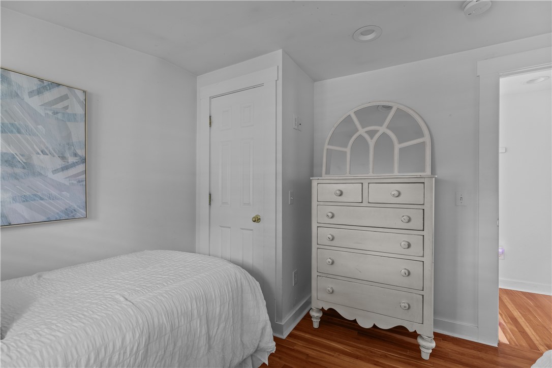 Bedroom with a white bed, arched-mirror dresser, abstract artwork, and hardwood floors.