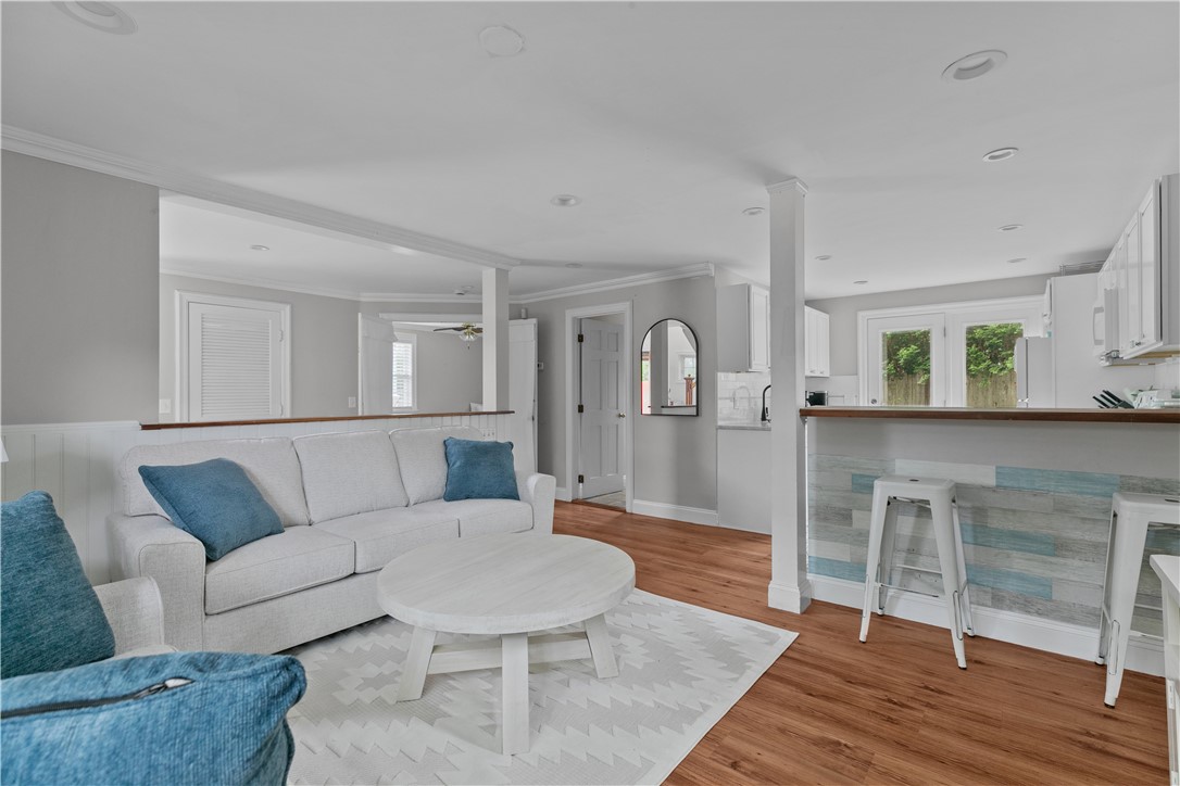 Open-plan living room with white sofa, blue accents, wood floors, and a kitchen breakfast bar.