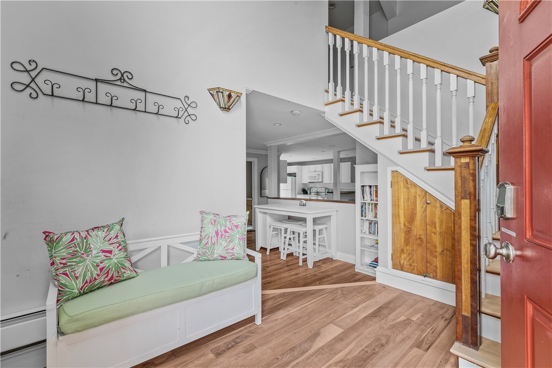 Entryway with a white staircase, under-stair wooden cupboard, cushioned bench, and kitchen island beyond.