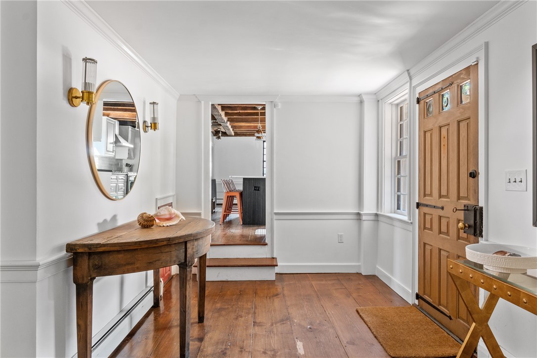 Entry foyer with wide-plank floors, a wood front door, and a rustic console table beneath an oval mirror.