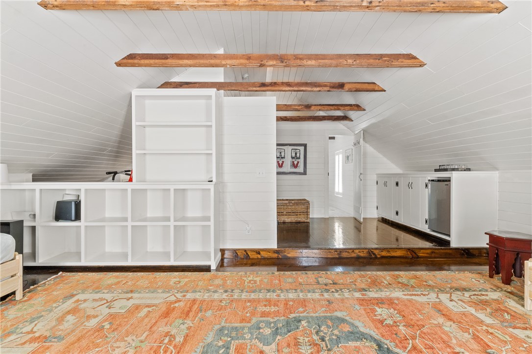 Attic kitchen with white cabinets, exposed wood beams, and a patterned rug.