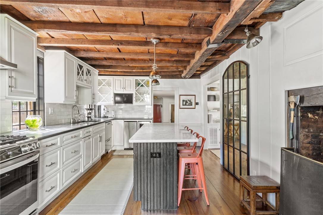 Kitchen with exposed timber ceiling beams, a marble island, and coral-colored stools.