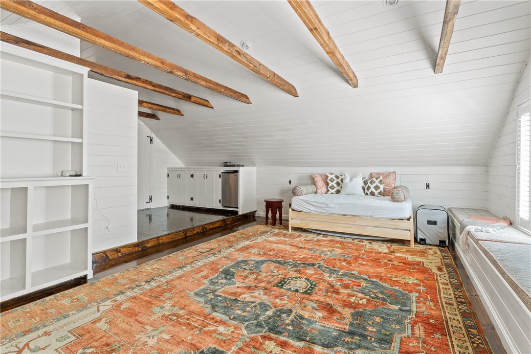 Attic bedroom with exposed wood beams, built-in cabinets, a daybed, and a large patterned rug.