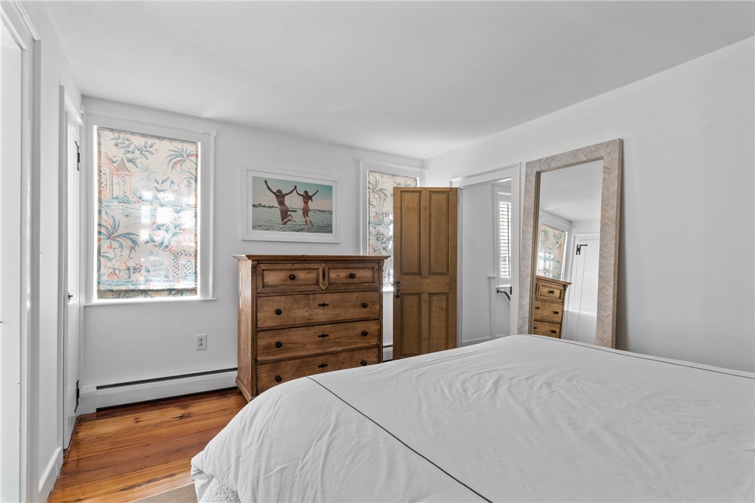 Bedroom with a white bed, wooden dresser, hardwood floors, and patterned window shades.