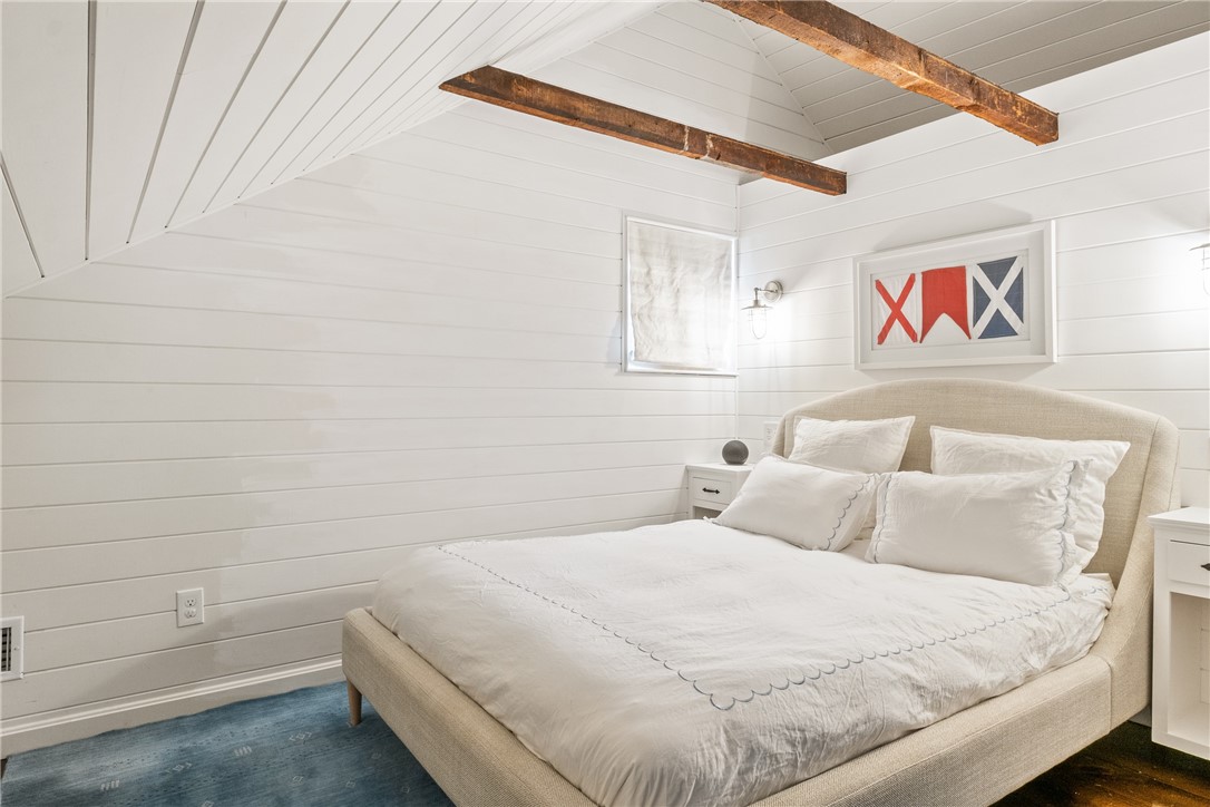 Bedroom with a large white bed, sloped shiplap ceiling, exposed beams, and blue carpet.