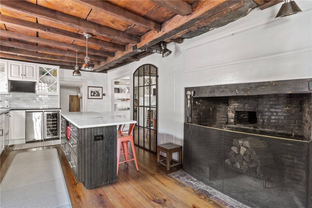 Kitchen with exposed timber ceiling beams, a large brick fireplace, and a dark island with red stools.