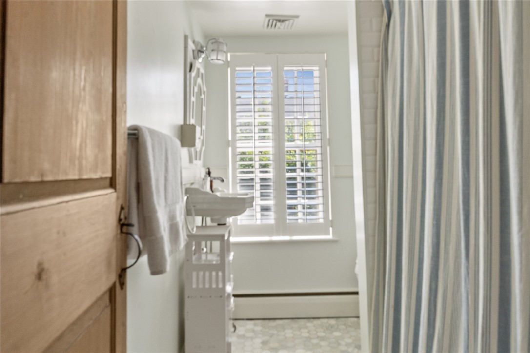 Bathroom with a pedestal sink, striped shower curtain, and shuttered window.