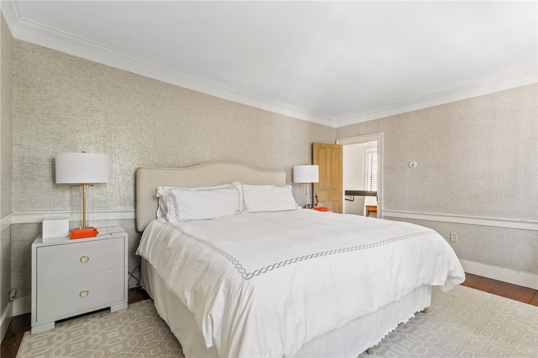 Furnished bedroom with a large white bed, neutral textured walls, and an open door to an adjoining room.