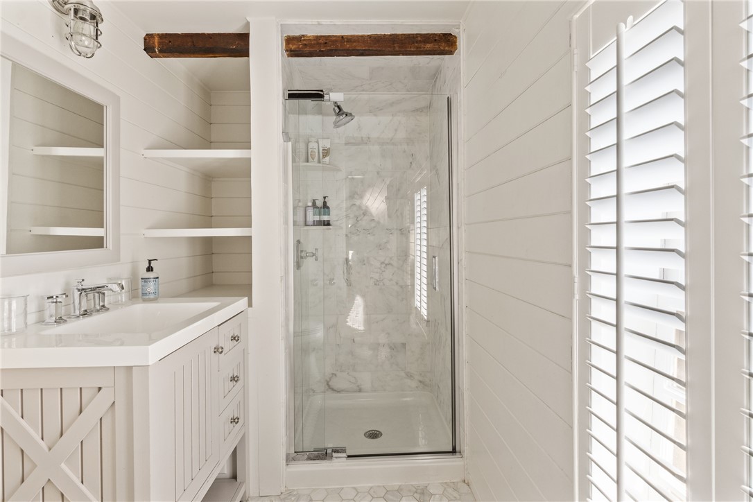 White bathroom with a marble shower, vanity, hexagonal tile floor, and plantation shutters.