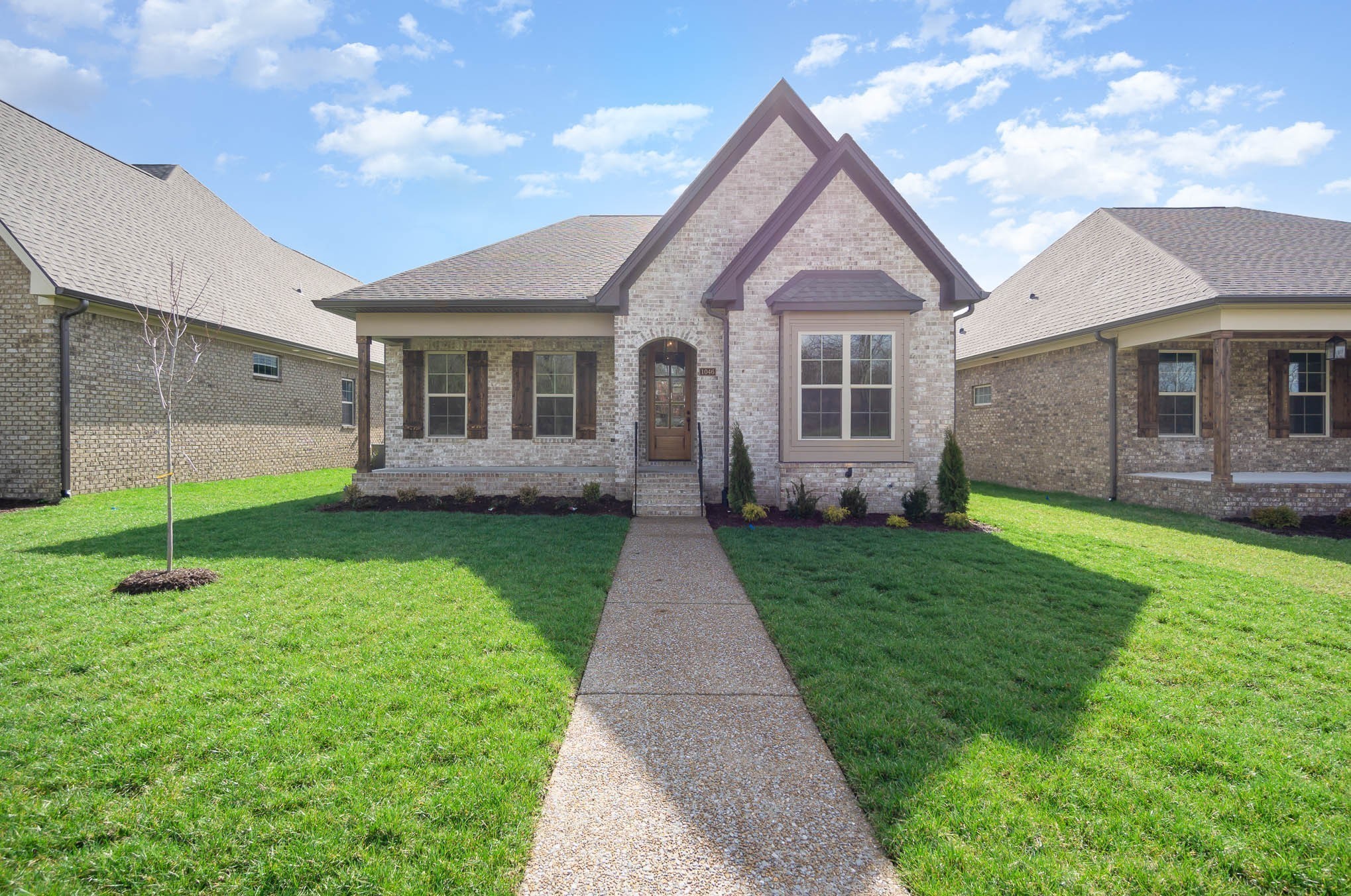 Brick home with prominent gables, covered porch, and walkway across a green lawn.