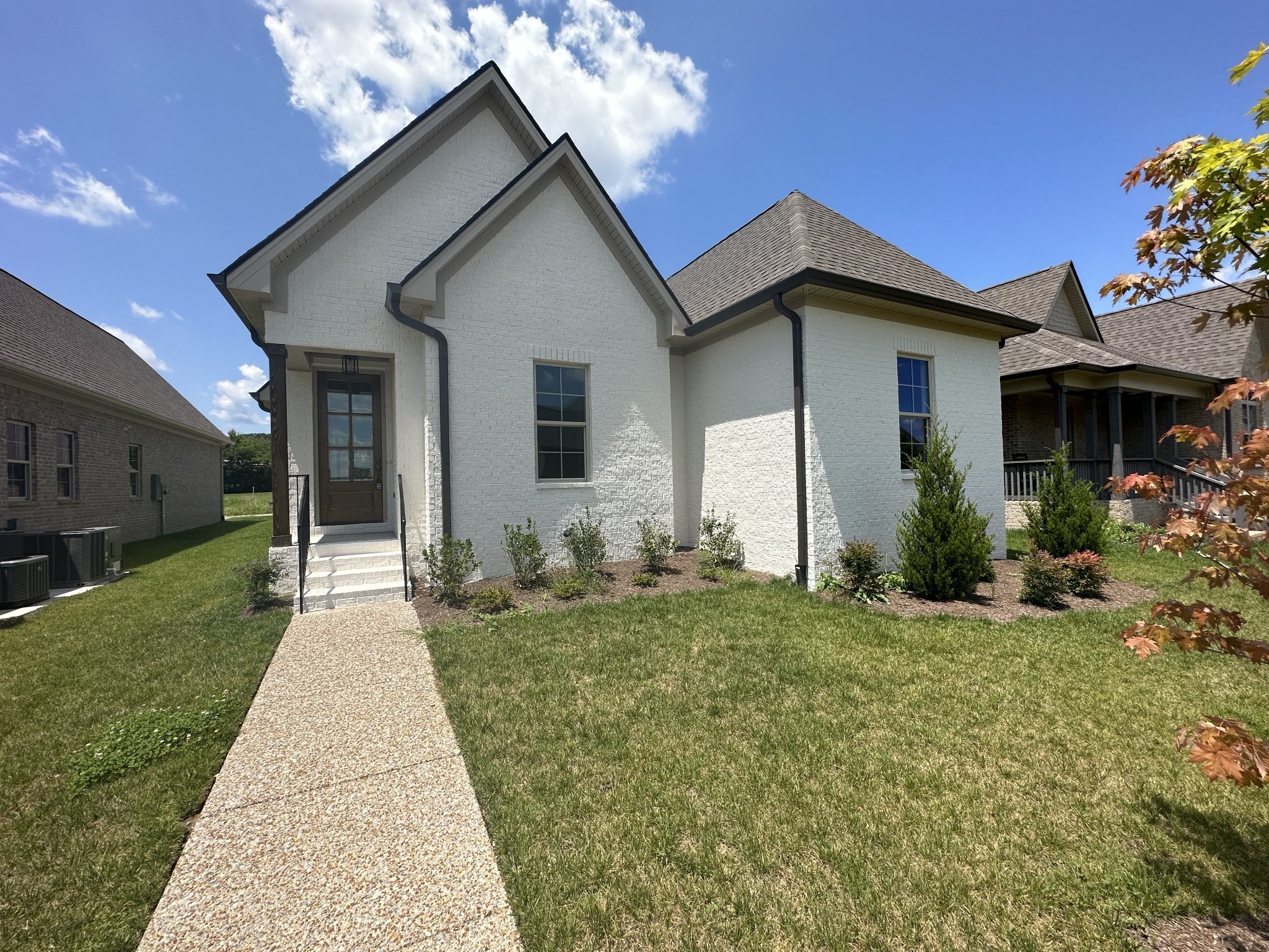 White brick home with steep gables, dark roof, and a pebble-finish walkway through the lawn.