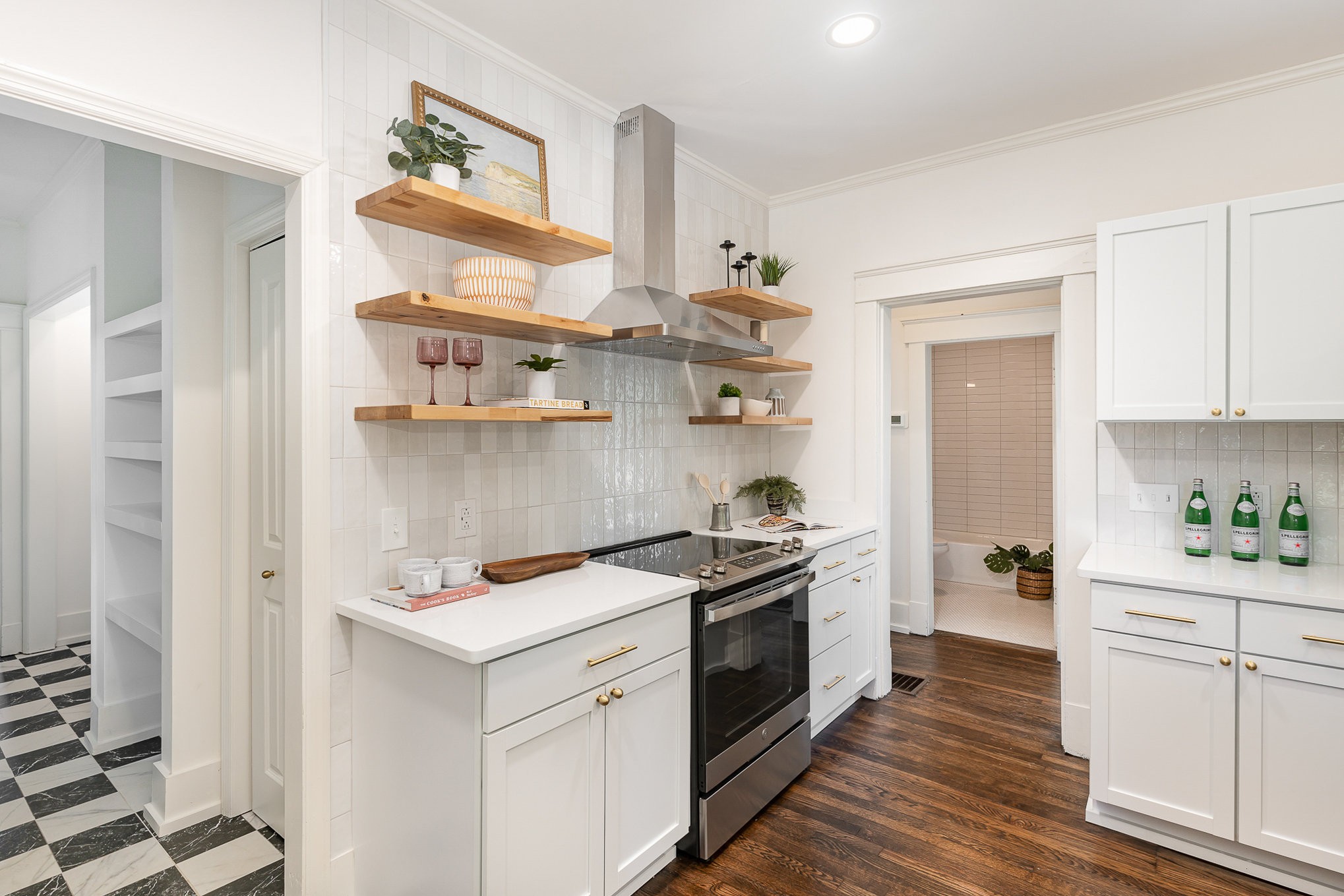 White kitchen with open wood shelves, brass hardware, and a stainless-steel range.