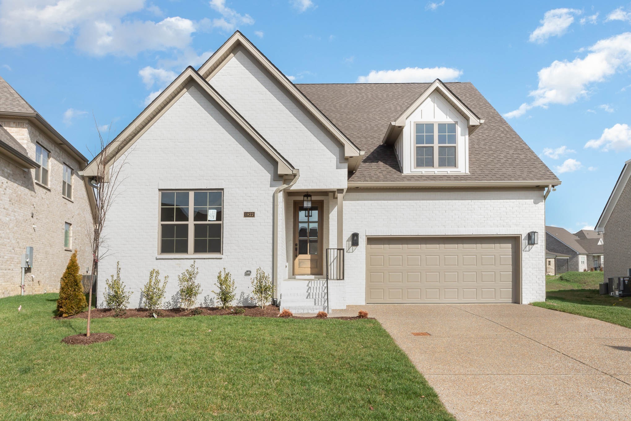 White-brick home with multiple gables, a tan double garage, and a green front lawn.