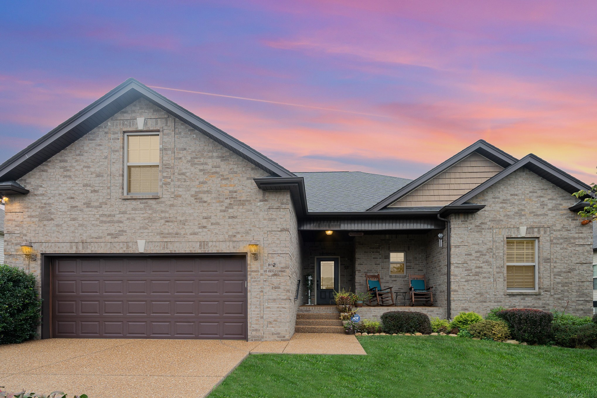 Brick home with a double garage and covered porch beneath a pink and orange dusk sky.