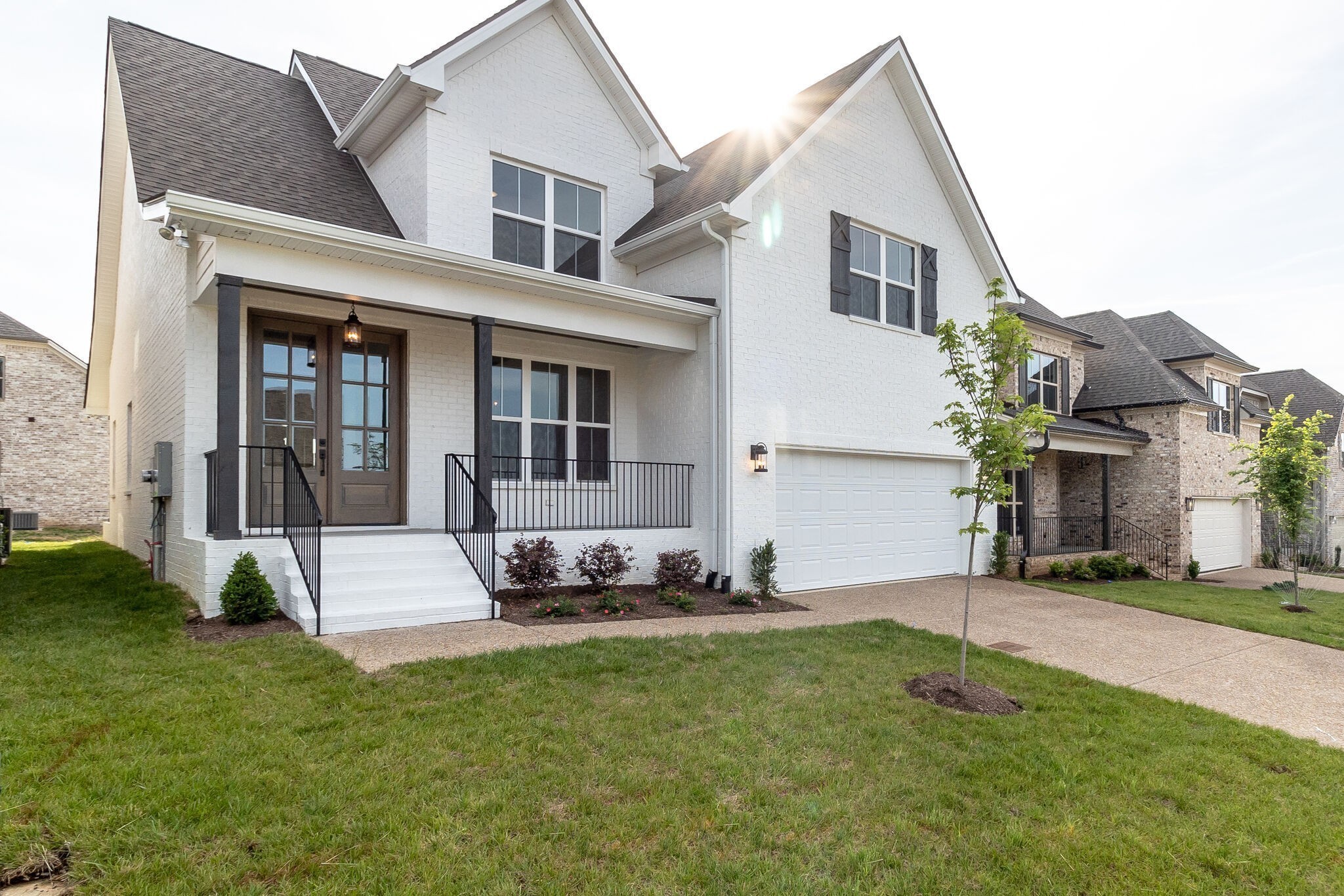 Two-story white brick house with a covered porch, black railings, and an attached garage.