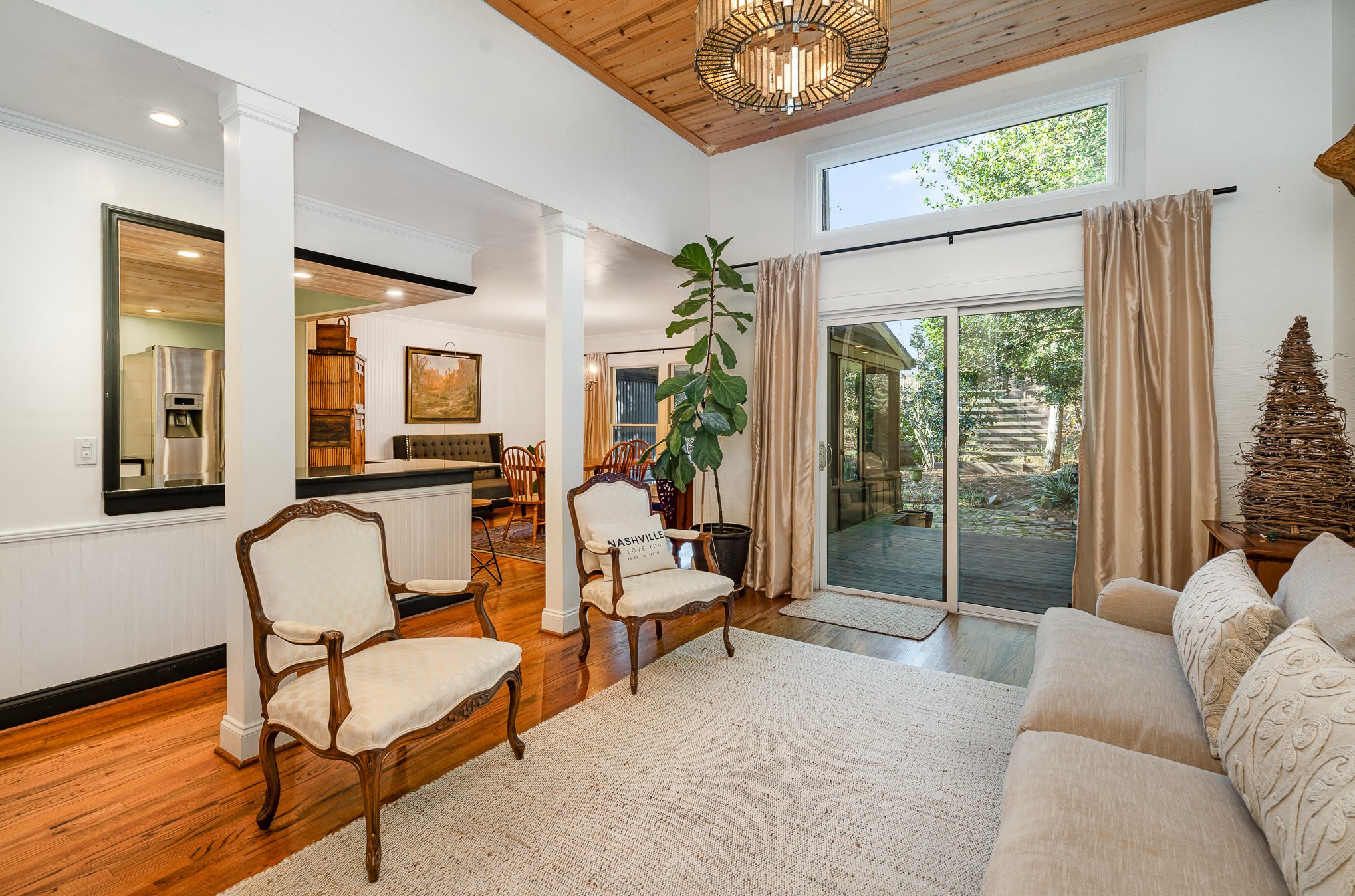 Living room with a wood-plank ceiling, carved armchairs, and sliding doors opening to a garden.