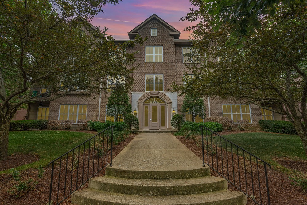 Brick residential building with a central entrance and broad front steps, framed by mature trees at dusk.