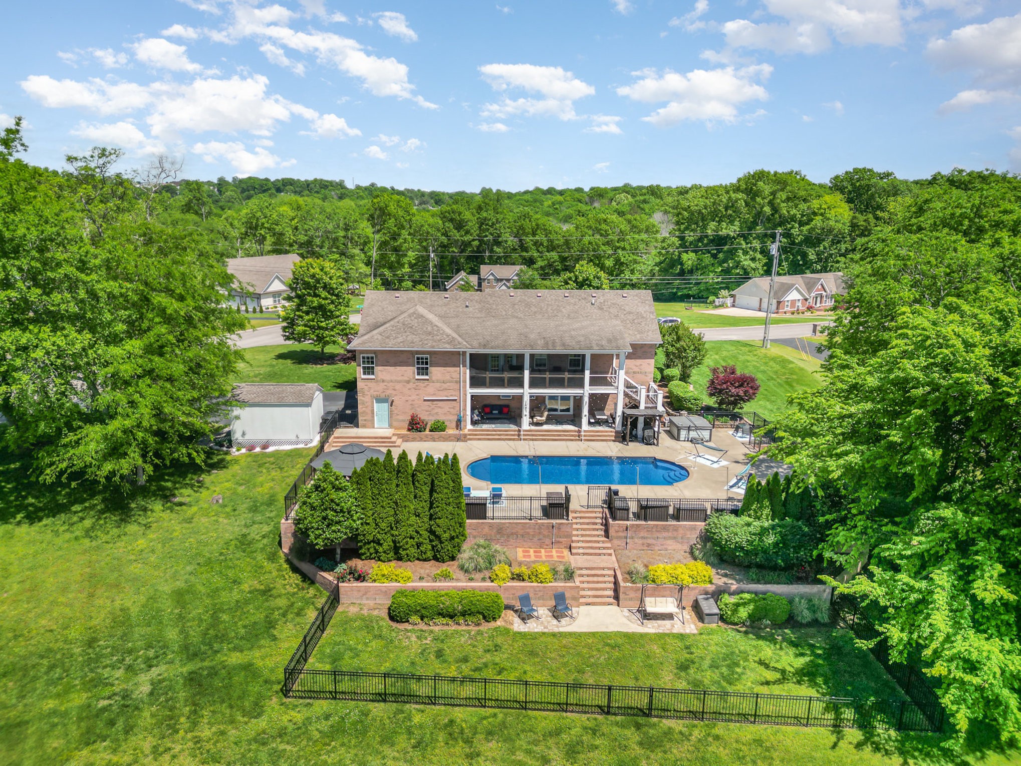 Aerial view of a brick home with a fenced yard, swimming pool, and landscaped patios.