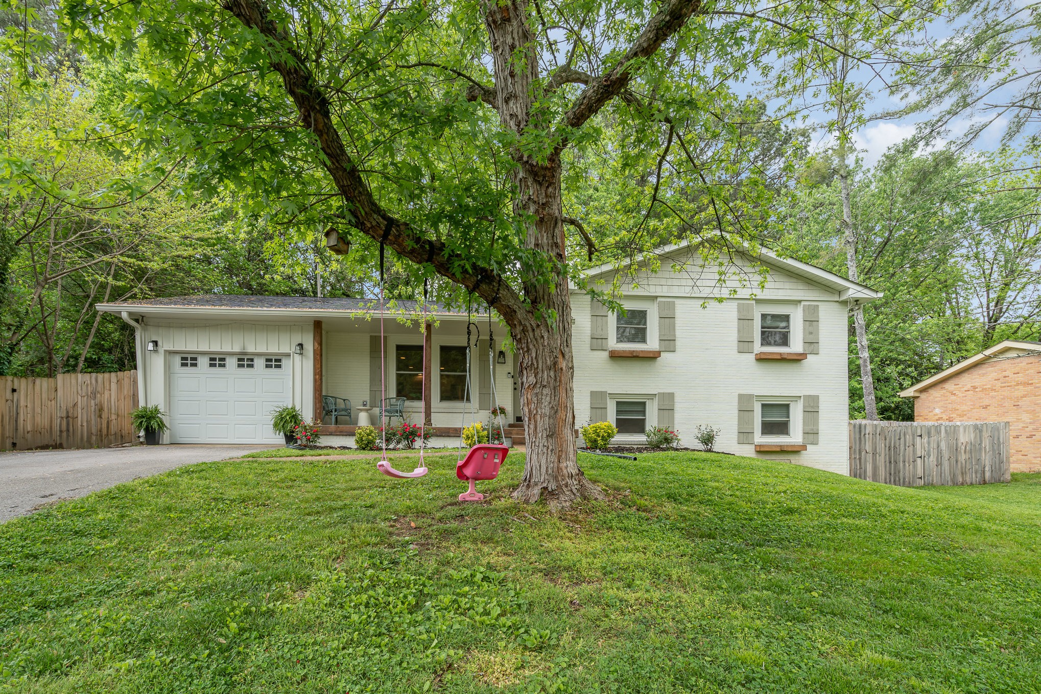 White split-level house with an attached garage and two swings hanging from a large front-yard tree.
