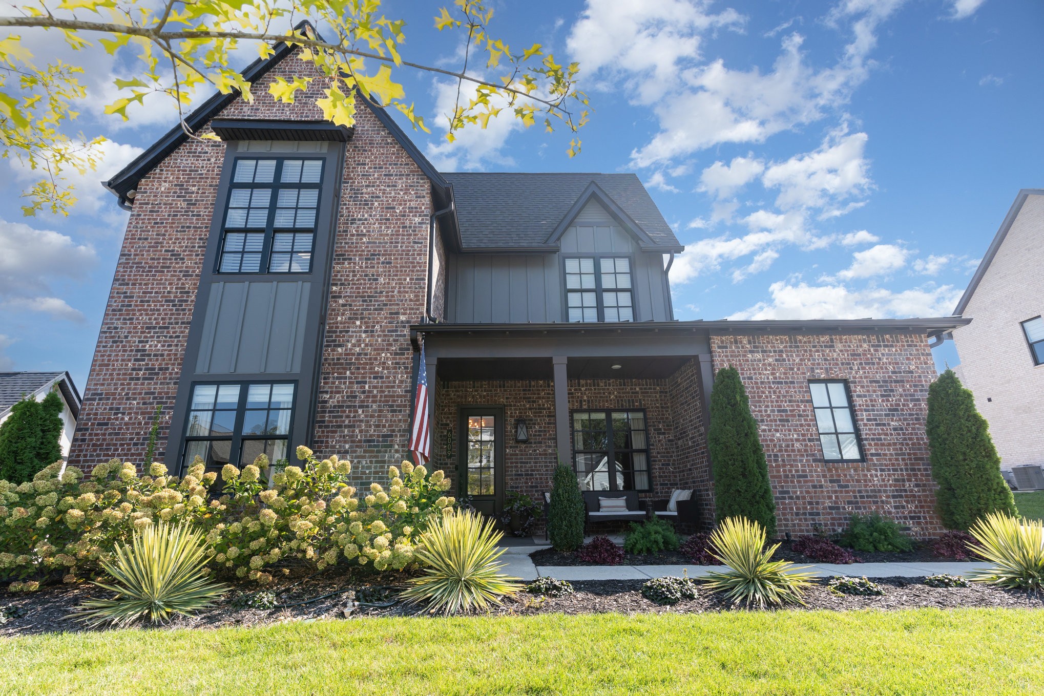 Two-story brick and gray-sided home with a covered porch and landscaped front yard