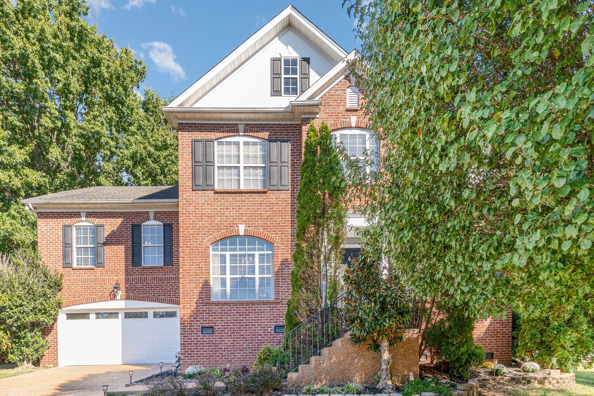 Two-story red brick house with white gable, attached garage, and landscaped front steps.